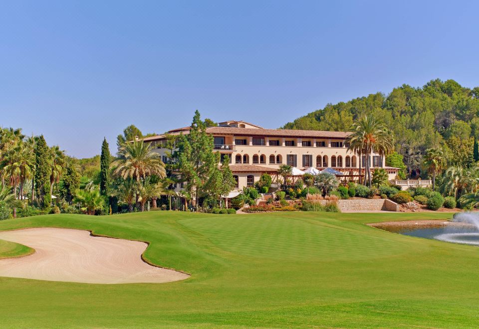 a large hotel surrounded by a lush green golf course , with trees in the background at Sheraton Mallorca Arabella Golf Hotel