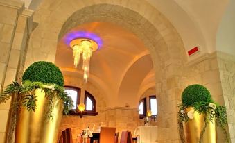 a grand dining room with marble floors , high ceilings , and large chandeliers , decorated with gold urns and green plants at Hotel Cenacolo