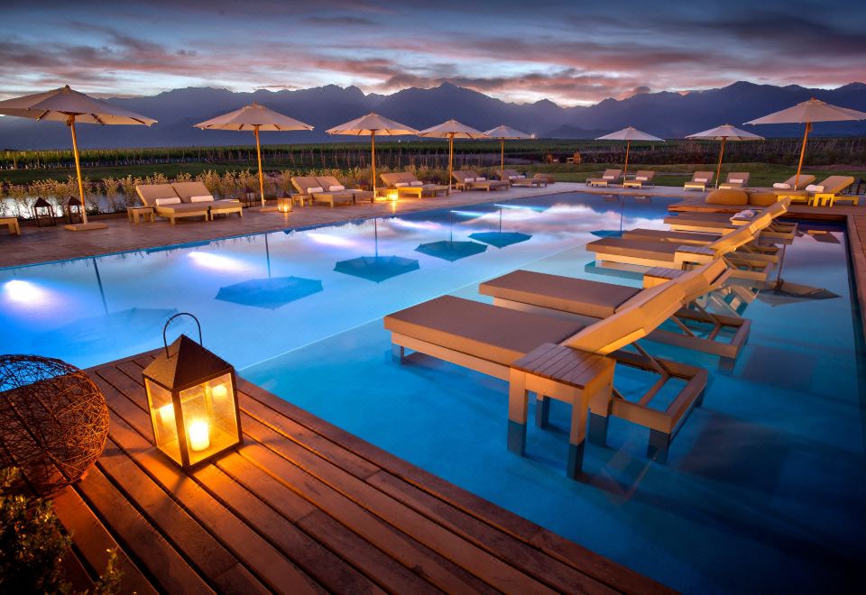 a large swimming pool with a wooden deck and lounge chairs , surrounded by mountains in the background at The Vines Resort & Spa