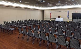 a large conference room with rows of black chairs and a flag on the stage at Grand Hotel