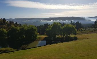 a beautiful landscape with rolling hills , a pond , and trees is bathed in sunlight from the setting sun at Nannup Hideaway