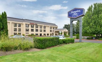 "a large hotel with a blue sign that says "" hampton inn "" is surrounded by green grass and bushes" at Hampton Inn Portland East
