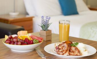 a table with a plate of food , a bowl of fruit , and a glass of orange juice at Gatton Motel