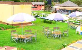 an outdoor dining area with umbrellas and chairs set up in a grassy area near a building at Lalanasi Lodge