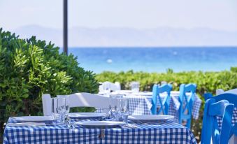 a dining table set with blue and white checkered tablecloth , chairs , and wine glasses , overlooking the ocean at Labranda Blue Bay Resort