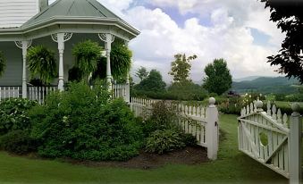a white gazebo surrounded by lush greenery and a white fence , with a blue sky in the background at Harmony Hill Bed & Breakfast