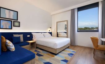 a modern hotel room with a large window , white bed , and blue accent wall , along with a wooden floor and blue accent at Hampton by Hilton Rome North Fiano Romano