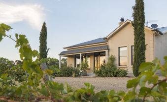 a beige house with a black roof and white trim is surrounded by greenery , under a clear blue sky at Barossa Shiraz Estate