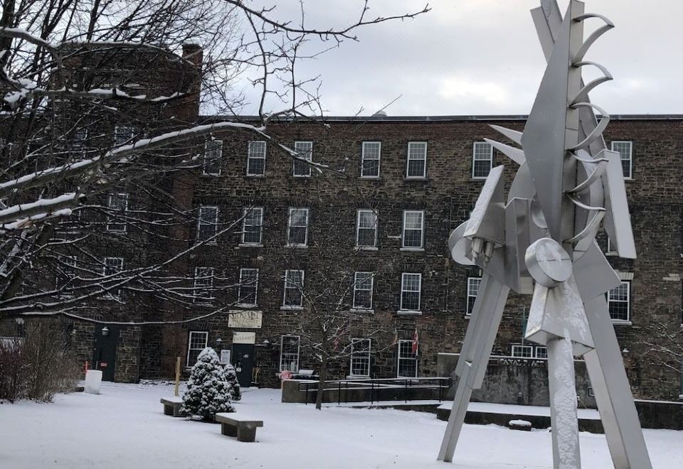 a snow - covered courtyard with a large metal sculpture in the middle , surrounded by snow - covered ground and trees at The Inn at Stone Mill