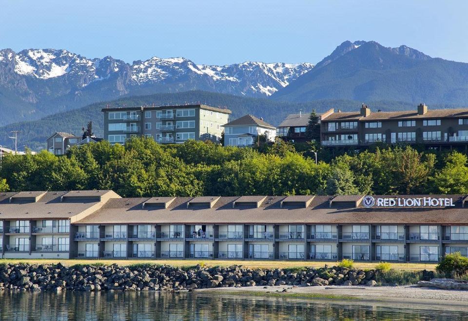 "a row of buildings with the word "" redcliff "" on them are situated near a body of water and snow - capped mountains in the background" at Red Lion Hotel Port Angeles Harbor