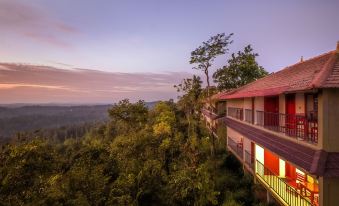 a multi - story building with a red roof is perched on the edge of a cliff , overlooking a forest at Coorg Cliffs Resort