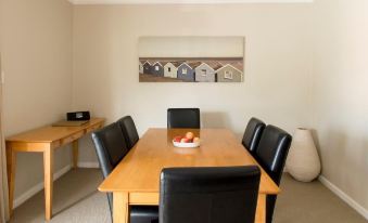 a dining room with a wooden table and black chairs , featuring a bowl of fruit on the table at The Marina Hotel - Mindarie