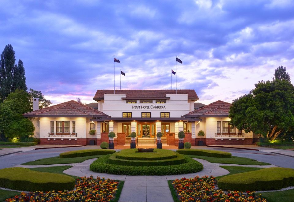 "a large white building with the sign "" the club "" on top , surrounded by lush greenery and flowers" at Hyatt Hotel Canberra - A Park Hyatt Hotel