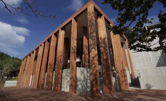 a modern wooden building with multiple levels and a central entrance , situated in a courtyard under a blue sky at The Naka Phuket