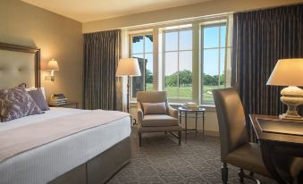 a hotel room with a king - sized bed , a chair , and a window overlooking a golf course at The Sewanee Inn