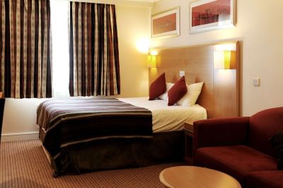 a large bed with a brown headboard is in the middle of a room with two lamps on either side at Village Hotel Liverpool