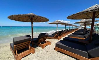 a row of wooden lounge chairs and umbrellas on a beach , with clear blue water in the background at Royal Hotel and Suites