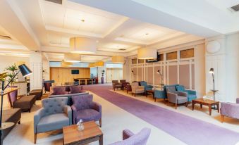 a modern , well - lit room with purple carpeting and blue armchairs , wooden tables , and large windows at The Golden Jubilee Hotel