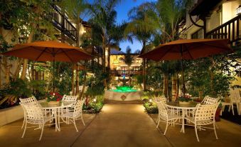 an outdoor dining area with white chairs and umbrellas , surrounded by palm trees and a pool at Best Western Plus Carpinteria Inn