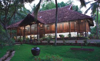a large wooden house surrounded by a lush green lawn , with several palm trees in the background at Somatheeram Ayurveda Village