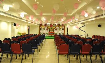 a large room with rows of red chairs and a stage decorated with pink balloons at Hotel Midcity