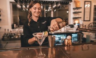 a woman in a black shirt is standing behind a bar , holding a martini glass and pouring a drink into it at Inn on Water Street