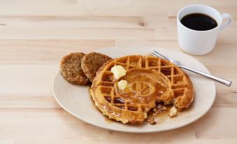 a plate of waffles with syrup , butter , and a biscuit on a wooden table , accompanied by a cup of coffee at Drury Inn & Suites St. Louis Airport