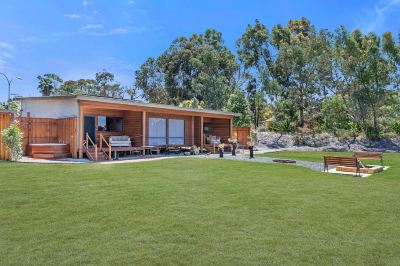 a wooden cabin surrounded by green grass and trees , with a pool in the background at The Swan Valley Retreat