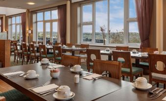 a large dining room with wooden tables and chairs , set for a meal , surrounded by windows offering a view of the city at The Telford Hotel, Spa & Golf Resort