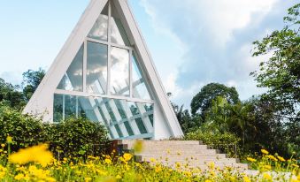 a white building with a triangular roof is surrounded by yellow flowers and green plants at Horison Green Forest Bandung