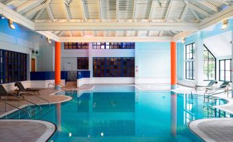 an indoor swimming pool with a blue and white color scheme , surrounded by white walls and columns at Forest of Arden Country Club
