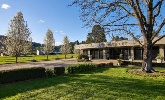 a large , well - maintained house surrounded by a lush green lawn , with trees and mountains in the background at Myrtleford Motel on Alpine