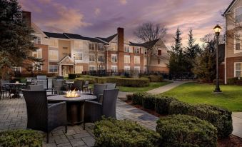 an outdoor dining area with tables and chairs , a fire pit , and a large building in the background at Residence Inn Saddle River