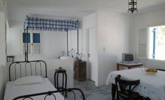 a white bedroom with two twin beds , a dining table , and a television in the corner at Angelica