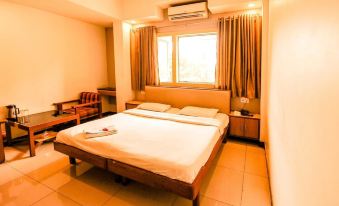 a large bed with white sheets is in a room with a chair and window at Hotel Sangam