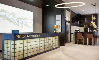 a hotel lobby with a check - in desk and a reception area , where a receptionist is standing at Hilton Garden Inn Zurich Limmattal