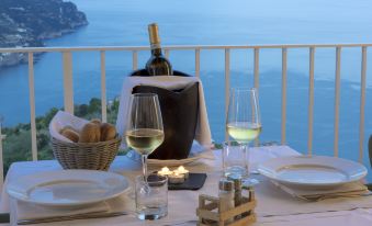 a table set for two with wine glasses , a bottle of wine , and a vase on a balcony overlooking the ocean at Villa Piedimonte