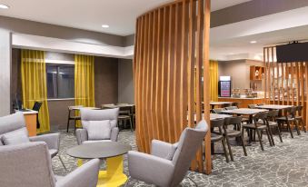 a modern hotel lobby with a wooden divider , gray chairs , and yellow curtains , as well as an orange bar in the background at SpringHill Suites Cleveland Solon