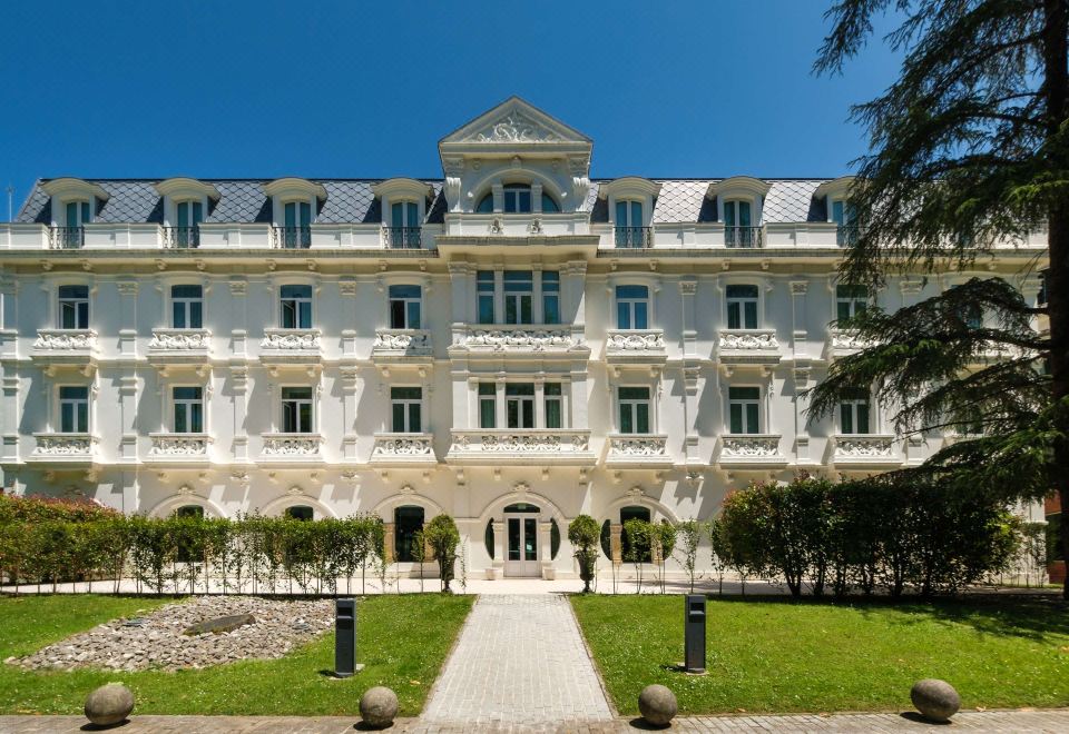 a large white hotel building with multiple balconies and windows , surrounded by trees and grass at Castilla Termal Solares