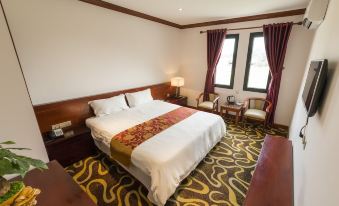 a large bed with white linens and a red and gold blanket is in the middle of a room with two windows at Hoang Trung Hotel