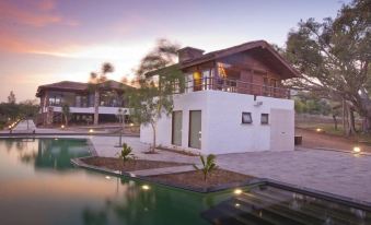 a modern , two - story house with a balcony and swimming pool , surrounded by lush greenery and clear water at The Serai Bandipur