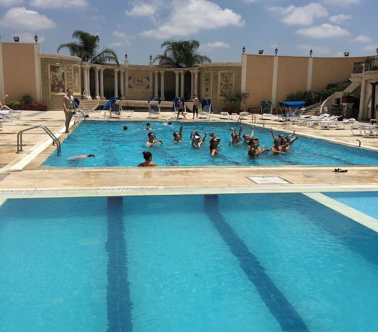 a group of people swimming in a large outdoor pool , with some of them wearing life jackets at Platinum Hotel