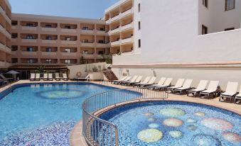 a large outdoor swimming pool surrounded by a building , with lounge chairs and umbrellas placed around the pool at Invisa Hotel la Cala