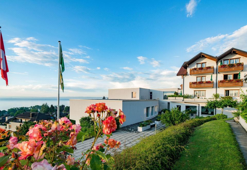 a modern white building with a green roof and balconies , surrounded by lush greenery and flowers at Best Western Hotel Rebstock