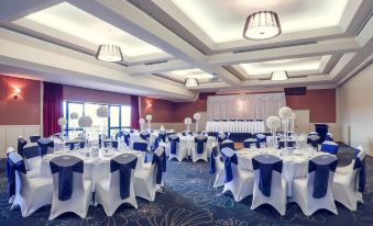 a large banquet hall is set up for a formal event , with multiple tables covered in white tablecloths and chairs arranged around them at Mercure Gold Coast Resort