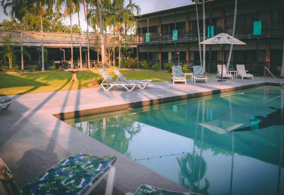a resort with a large swimming pool surrounded by lounge chairs and umbrellas , as well as palm trees at Litchfield Outback Resort