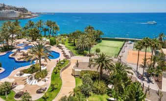 a bird 's eye view of a resort with pool , palm trees , and tennis courts near the ocean at Radisson Blu Resort, Gran Canaria