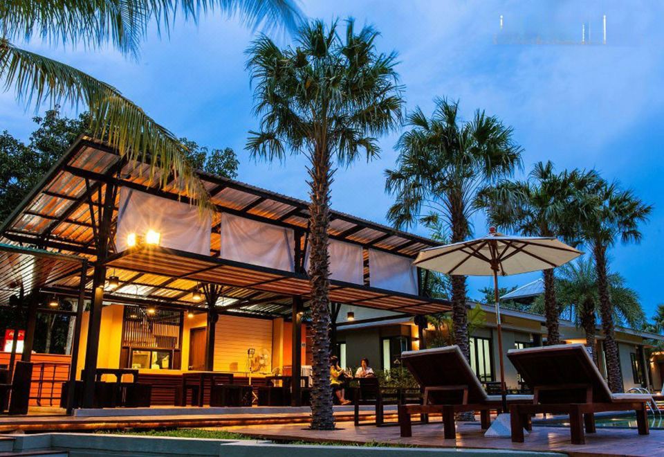a large , modern building with a bar and outdoor seating area , surrounded by palm trees at dusk at Aroonsawad Riverview Resort