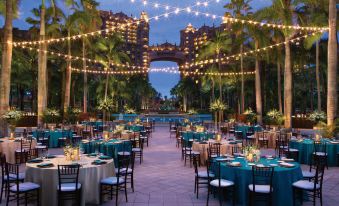 a large outdoor event with multiple tables set up for a formal dinner , surrounded by palm trees and lights at The Royal at Atlantis