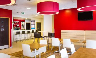 a modern restaurant with red walls , white tables and chairs , and a bar area under red pendant lights at Travelodge Norwich Central Riverside
